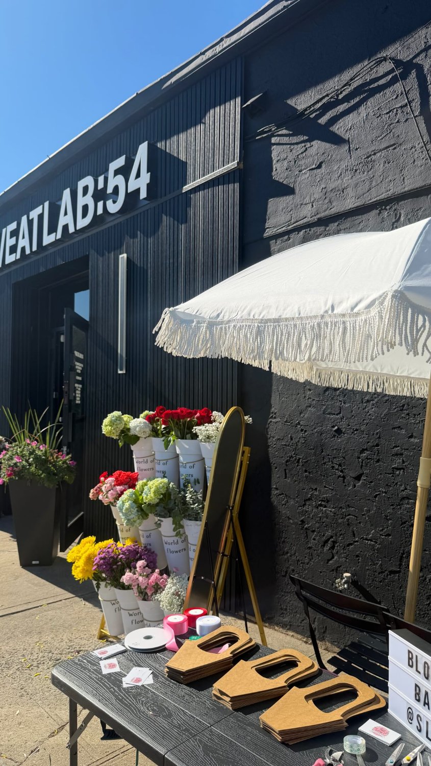 AYM's Flower Bar pop-up: buckets of fresh flowers under a fringed umbrella at a local event
