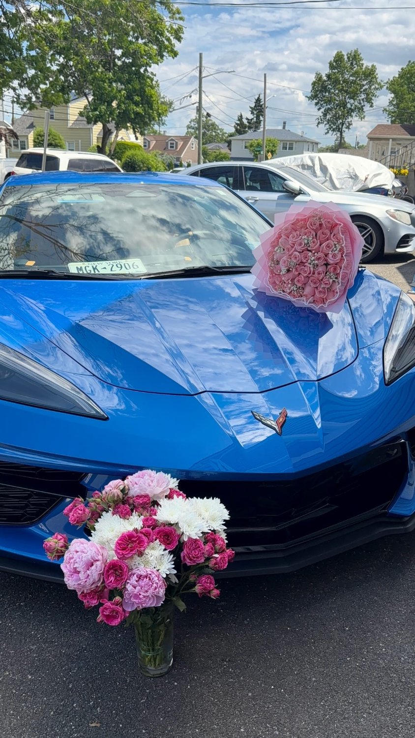 A bouquet delivered on the hood of a blue Corvette